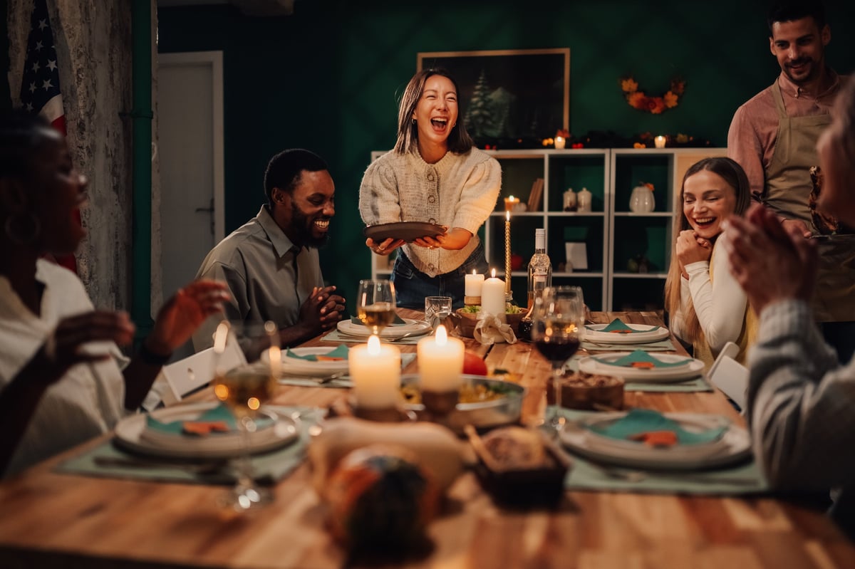A diverse group of adults sharing a family-style dinner together at a dining table in a warm, well-lit home